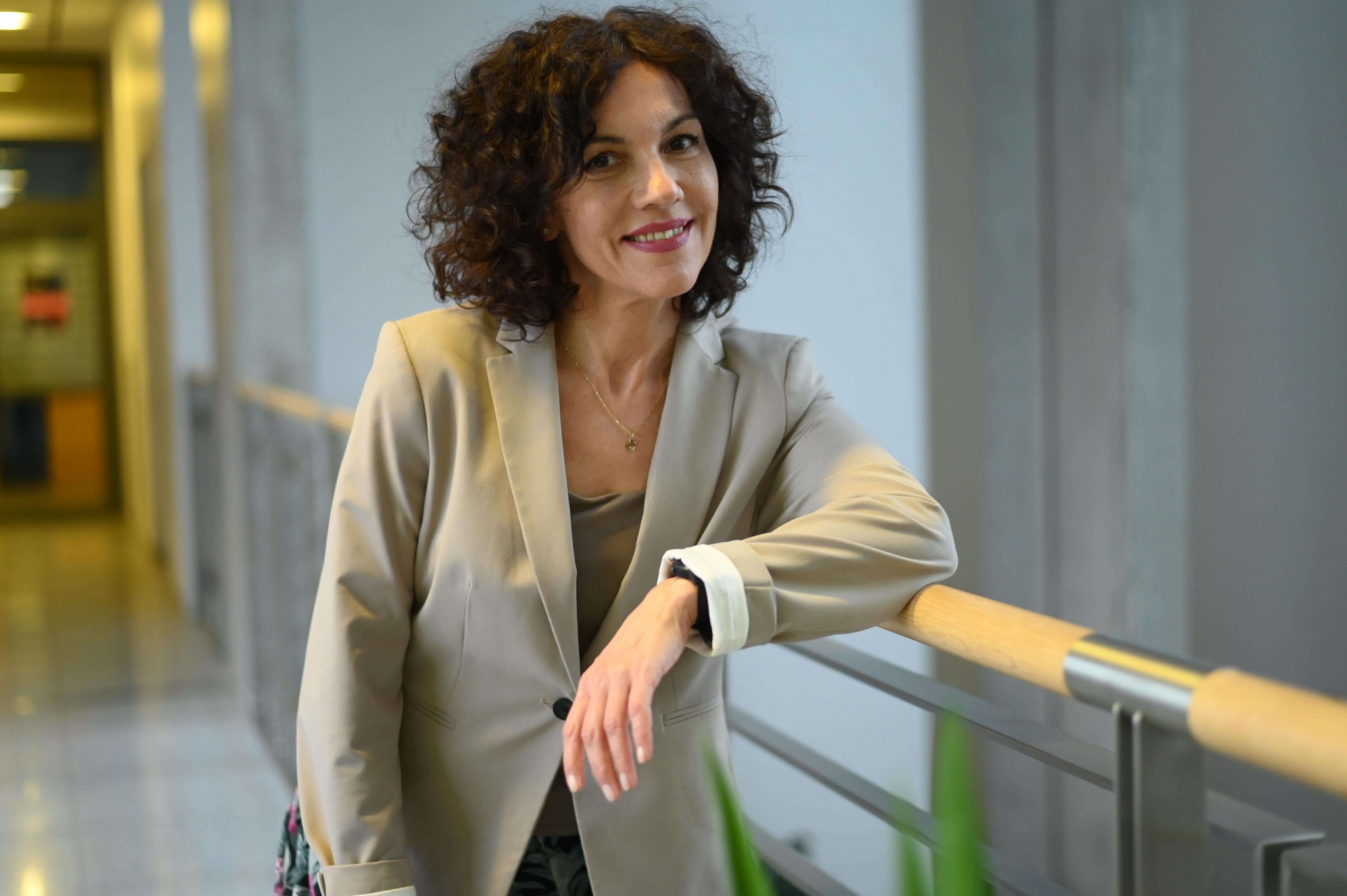 Zdjęcie Lidii Szutkowskiej w beżowej marynarce opartej o balustradę w jasnym wnętrzu biurowym.